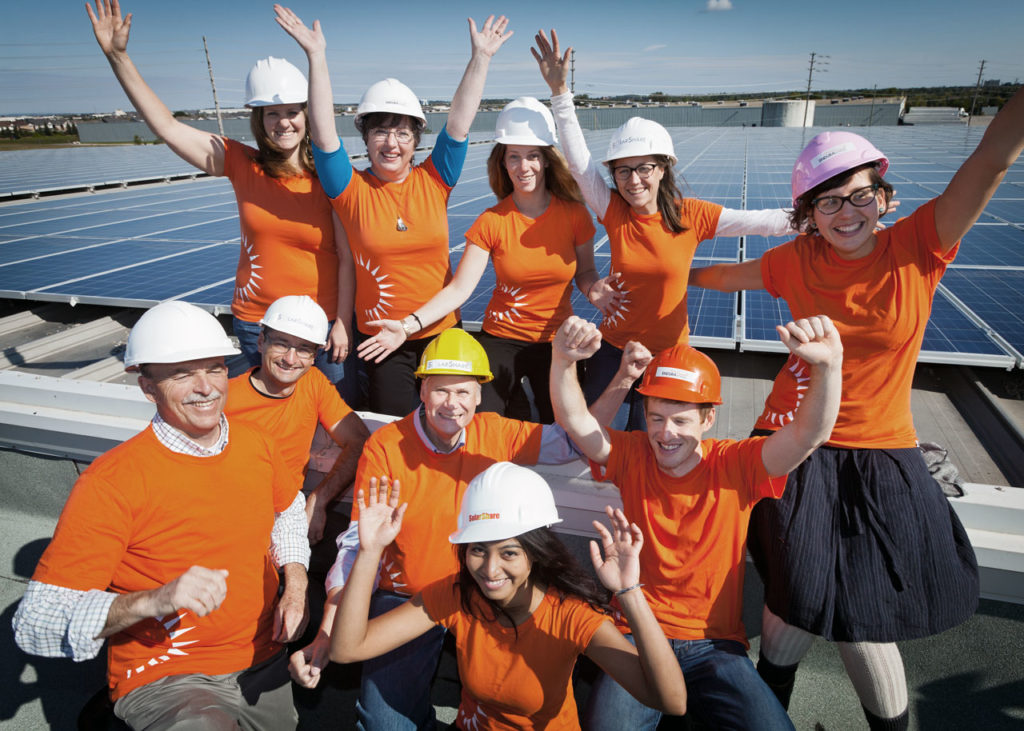 A group of people wearing orange shirts in front of solar panels