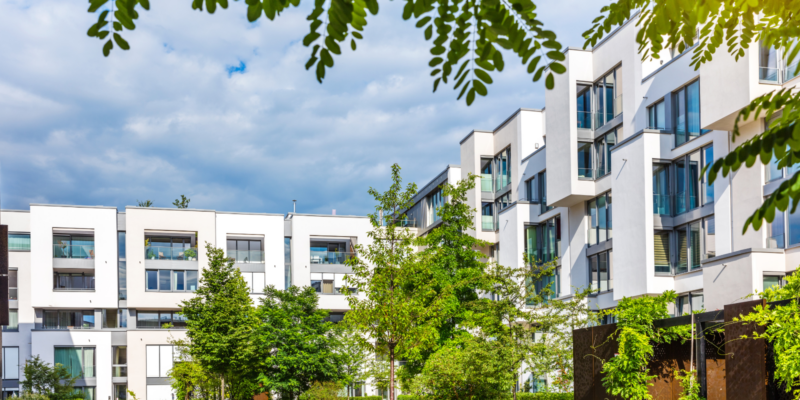 Modern white apartment buildings with many windows, like propolis hives, surrounded by green trees and clouds.