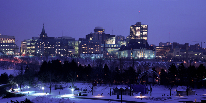 Snowy Ottawa cityscape at dusk with lit buildings and trees, viewed from a park with Ottawa Community Land Trust.