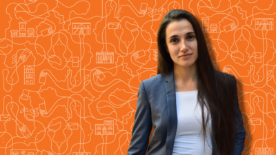 Woman in a gray blazer stands against an orange background, representing the spirit of impact investment.