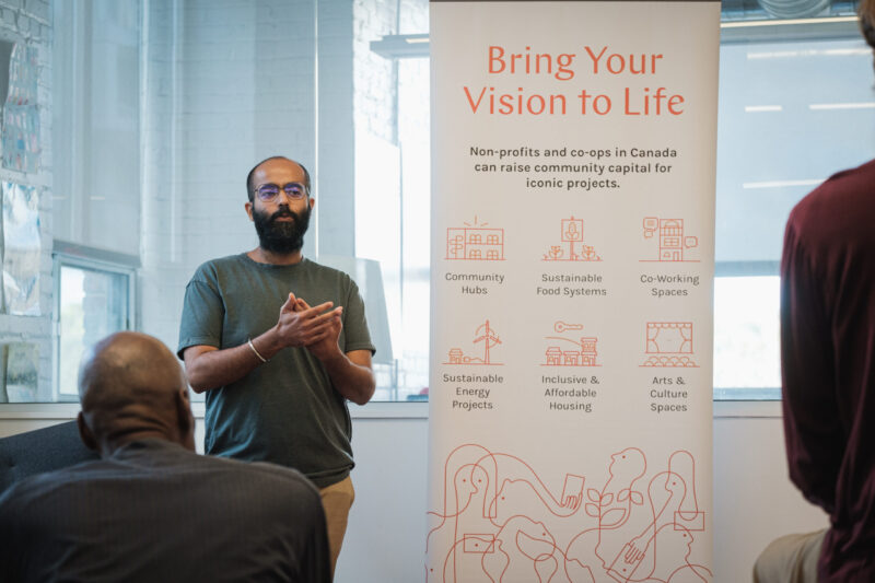 A man speaks in front of a Bring Your Vision to Life banner at a community meeting.