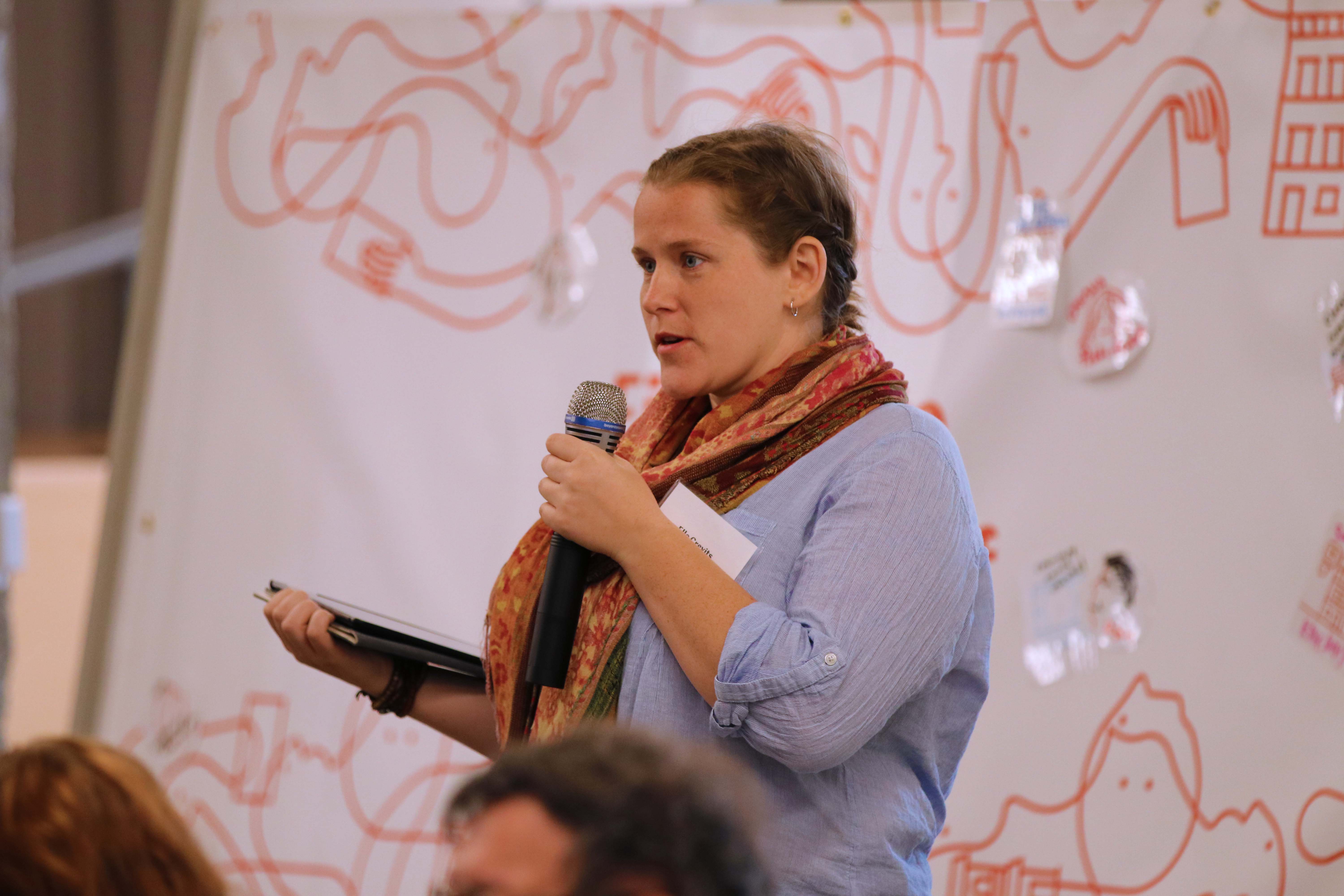 Someone speaking into a microphone in front of tapestry sign