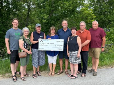 Eight people stand outdoors holding a $50,000 check, celebrating strong community bonds among lush greenery.