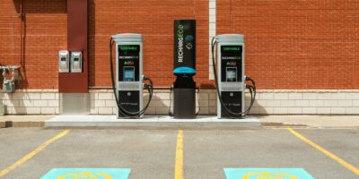 Two electric vehicle charging stations promote community bonds in front of a brick wall, with parking spots.