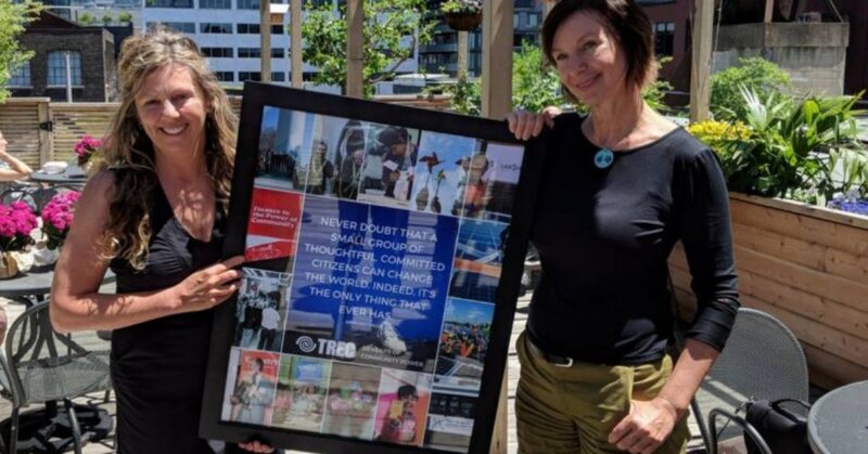 Two women stand outdoors, smiling, holding a framed collage presented by the Board of Directors.