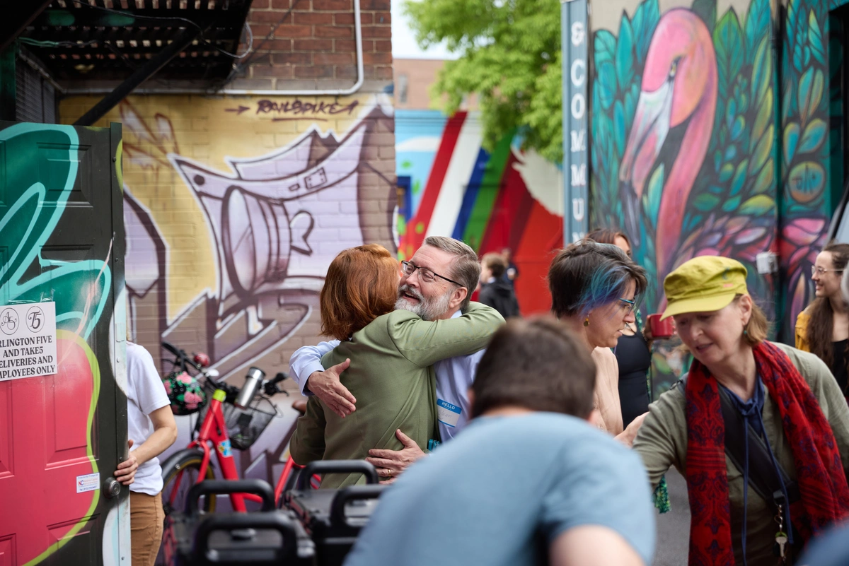 People hugging in a vibrant, graffiti-covered alley with others talking and walking nearby.