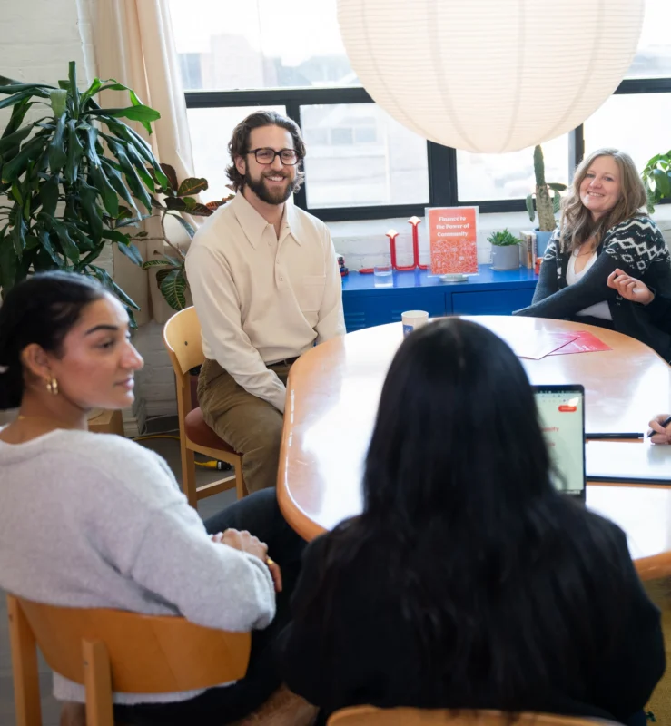 Quatre personnes sont assises autour d'une table ovale dans un bureau lumineux ; elles sourient et discutent entre elles.