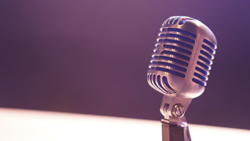 A vintage silver microphone stands against a blurred purple background, echoing the spirit of Inspirit Foundation.