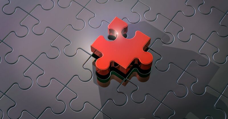 A shiny red puzzle piece hovers above a mostly completed gray puzzle, about to fit into place.