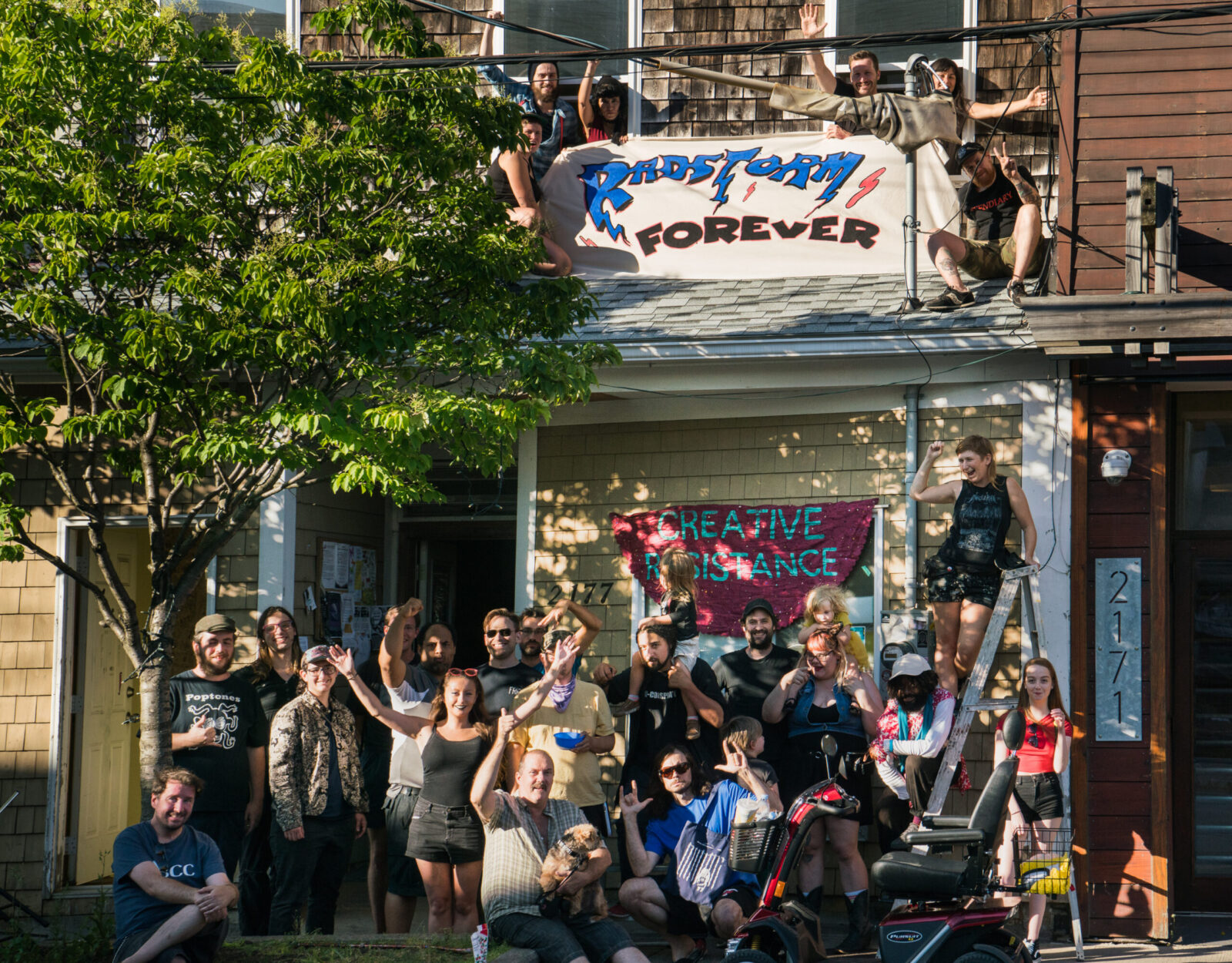 RadStorm members in front of the space, with two banners which read "RadStorm Forever" and "Creative Resistance."