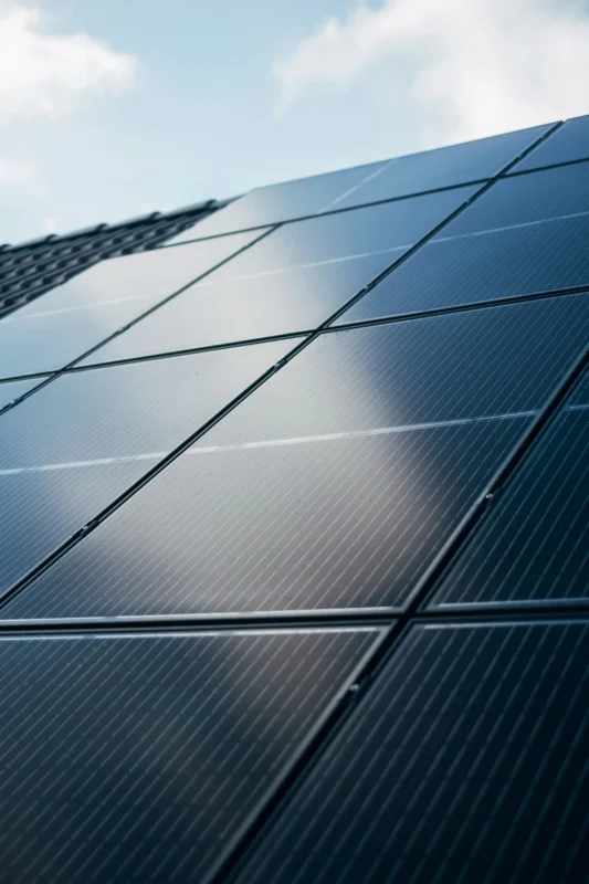 A close-up of solar panels on a rooftop under a partly cloudy sky, reflecting sunlight.