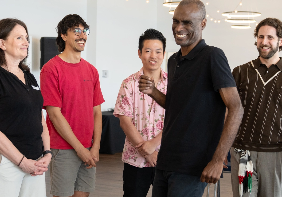 Five people stand indoors, smiling and laughing together in a casual, friendly setting.