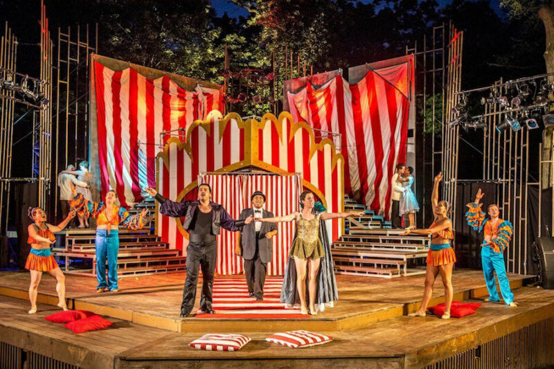 Des comédiens vêtus de costumes colorés se produisent sur une scène rayée aux allures de cirque, grâce à une augmentation des subventions accordées aux arts.